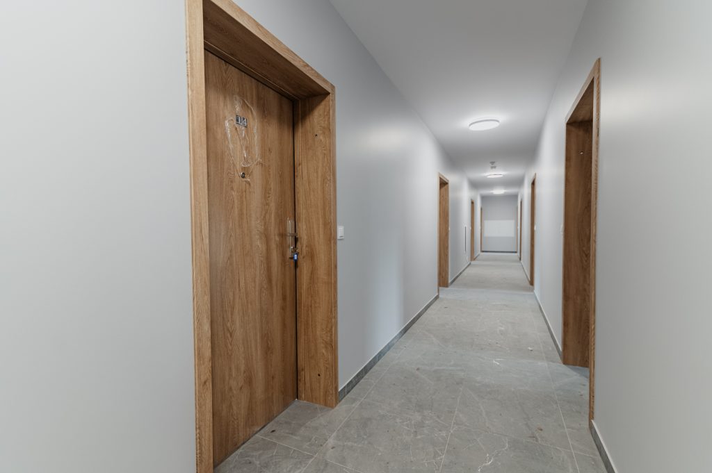 Wnętrze budynku D na Osiedlu Gwiazdowo – widok na jasny korytarz z zamontowanymi drzwiami wejściowymi do mieszkań.
