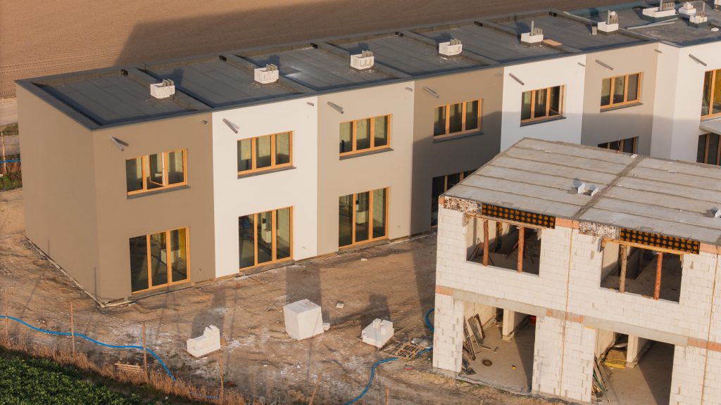 Widok z lotu ptaka na inwestycję Rabowice Park w Swarzędzu – gotowy budynek z elewacją i dużymi oknami oraz sąsiedni budynek w trakcie budowy z widoczną konstrukcją drugiej kondygnacji.