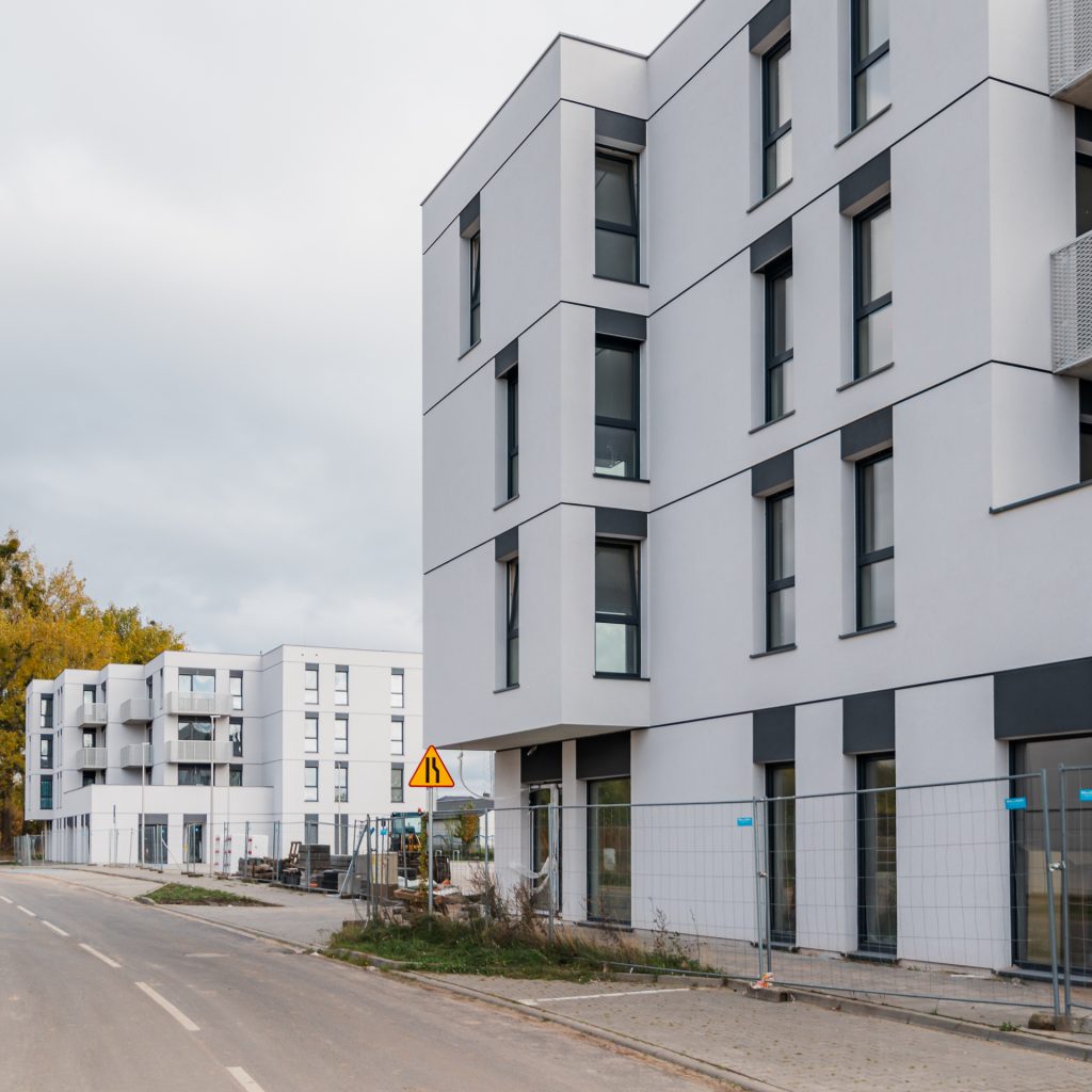 Widok z ulicy na nowoczesne budynki mieszkalne inwestycji Tarasy Rokietnicy. Biała elewacja z grafitowymi akcentami oraz wewnętrzna droga osiedlowa. Realizacja ogólnopolskiego dewelopera SOVO.