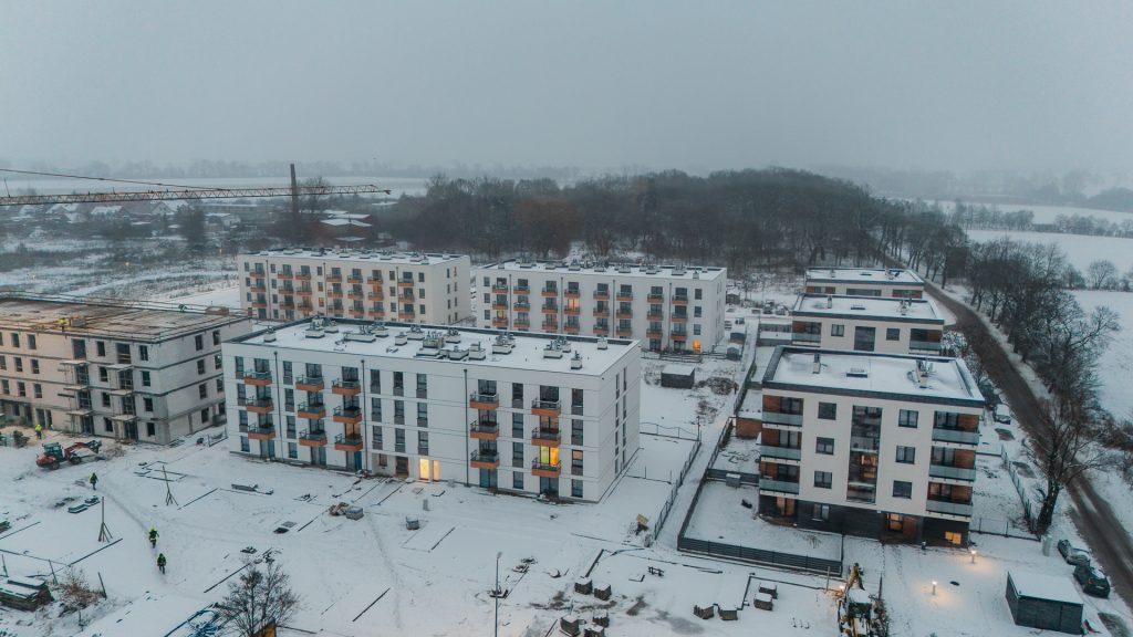 Osiedle Gwiazdowo zimą – widok z drona na gotowe budynki i budynek w trakcie budowy z żurawiem